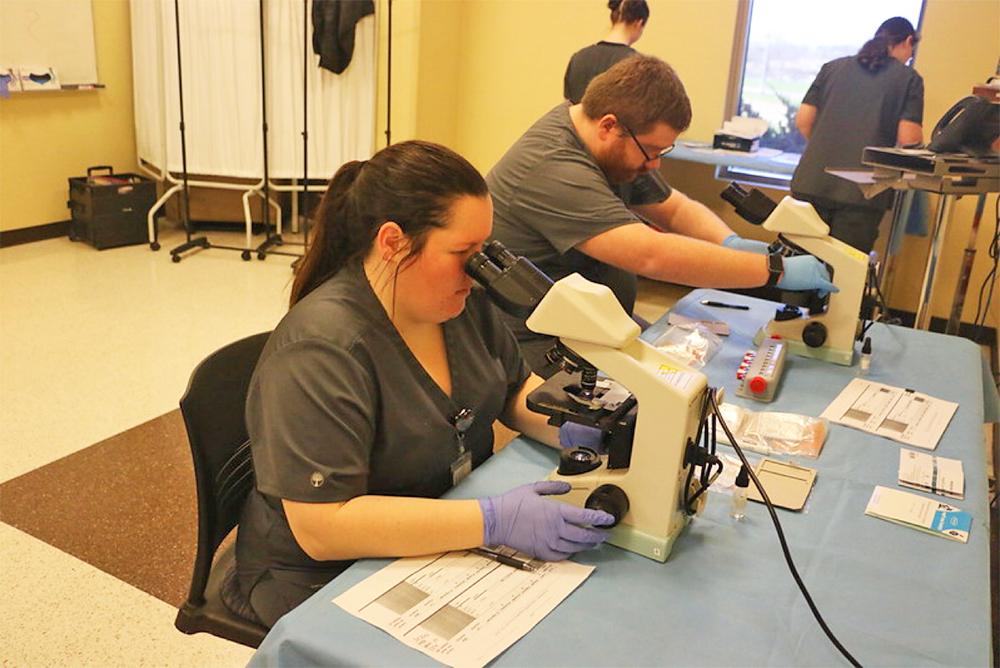 Students in the 澳门威尼斯人APP下载状态 社区 College MLT program look at collected samples through microscopes. 